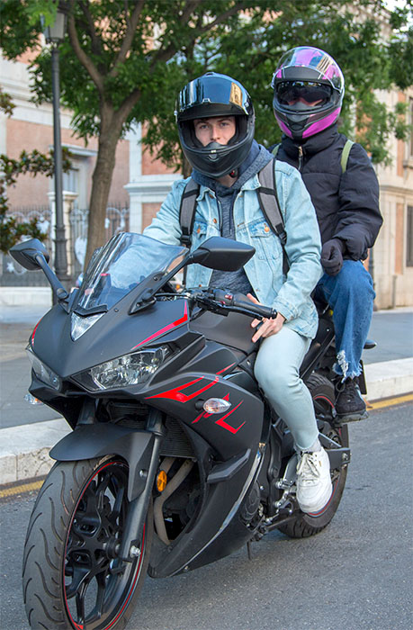 Two motorcyclists on a black sport motorcycle parked on a city street, both wearing helmets and jackets.